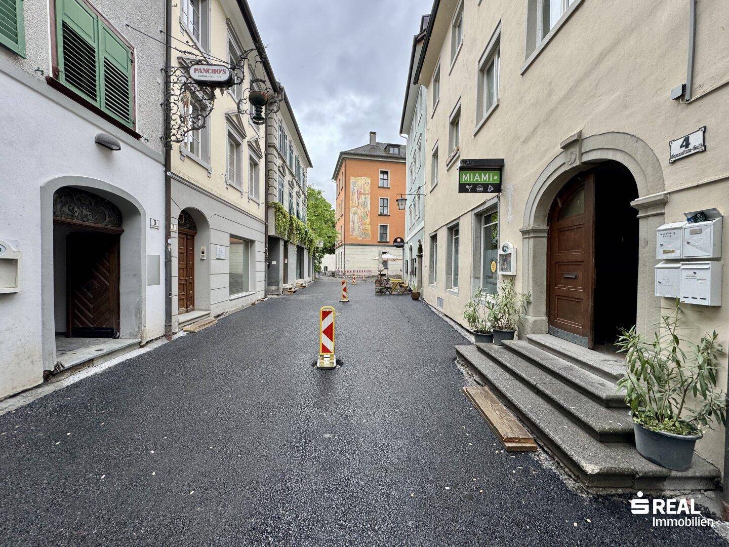 Enge Gasse in einer Altstadt mit historischen Gebäuden und Geschäften, gepflasterter Straße.