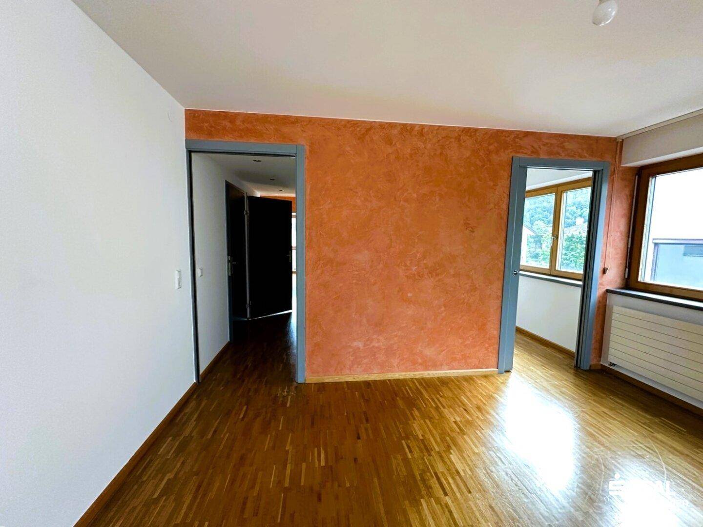 Flur mit auffälliger orangefarbener Akzentwand, Holzboden und Zugang zu weiteren Räumen.