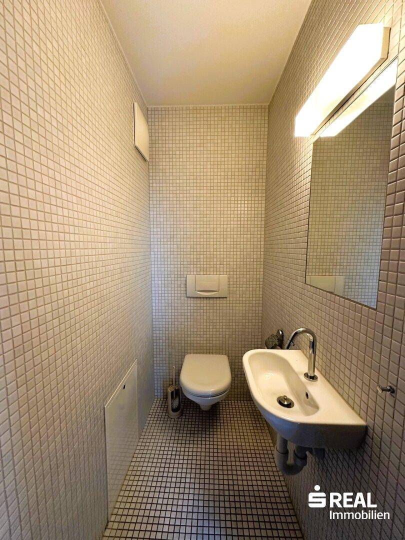 Kleines Gäste-WC mit weißen Mosaikfliesen an Wänden und Boden, inklusive Toilette und Waschbecken.