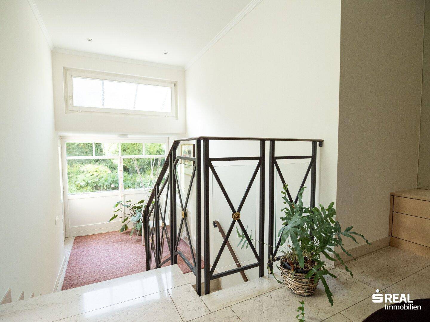 Heller Flur mit eleganter Marmortreppe und großen Fenstern, die viel Tageslicht hereinlassen.