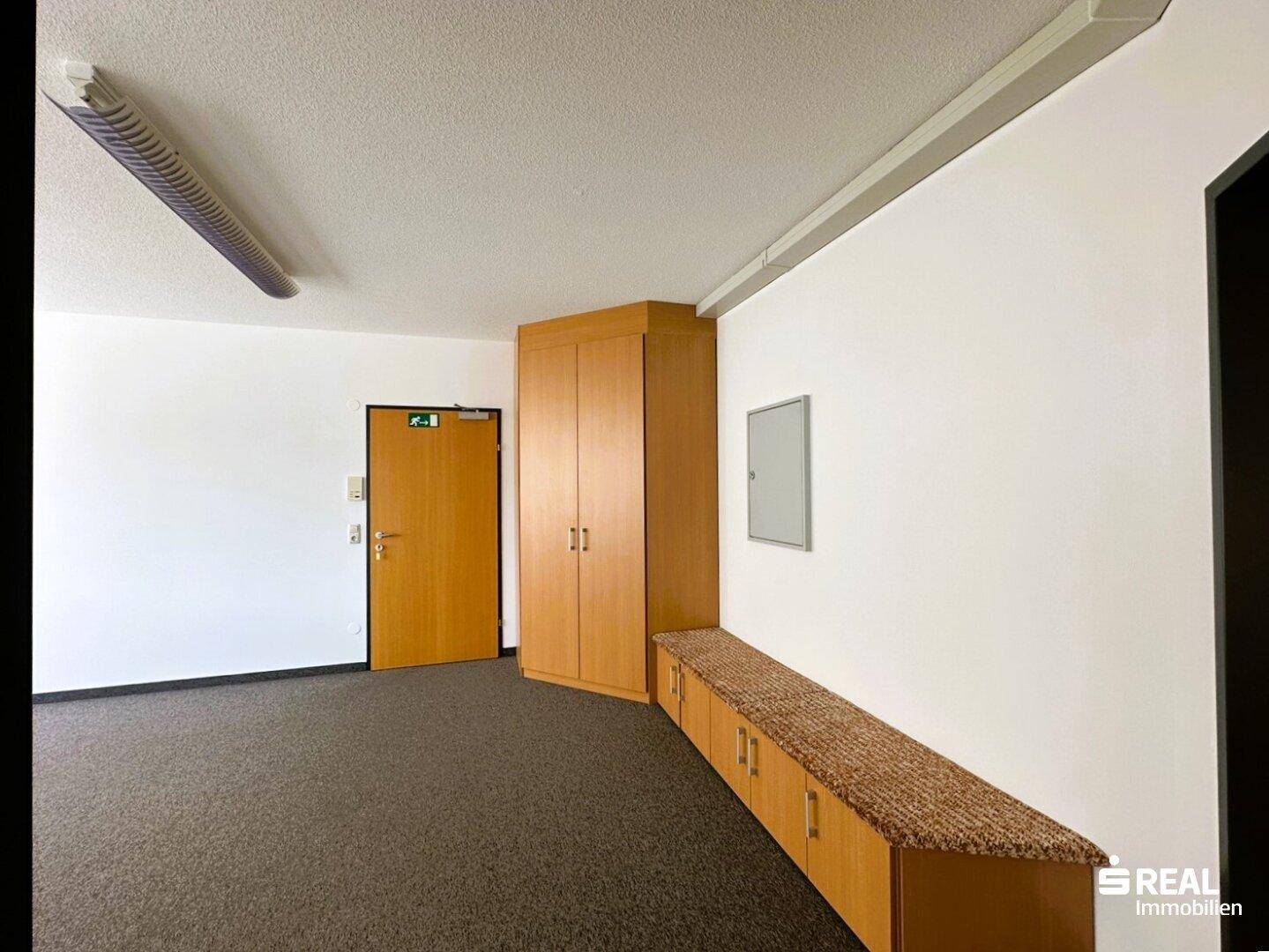 Büro mit Teppichboden, Holzschrank und einer langen Sitzbank mit Polsterung für zusätzlichen Komfort.