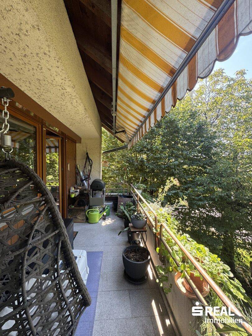 Geräumiger Balkon mit Hängesessel, vielen Pflanzen und einer Markise, umgeben von viel Grün.
