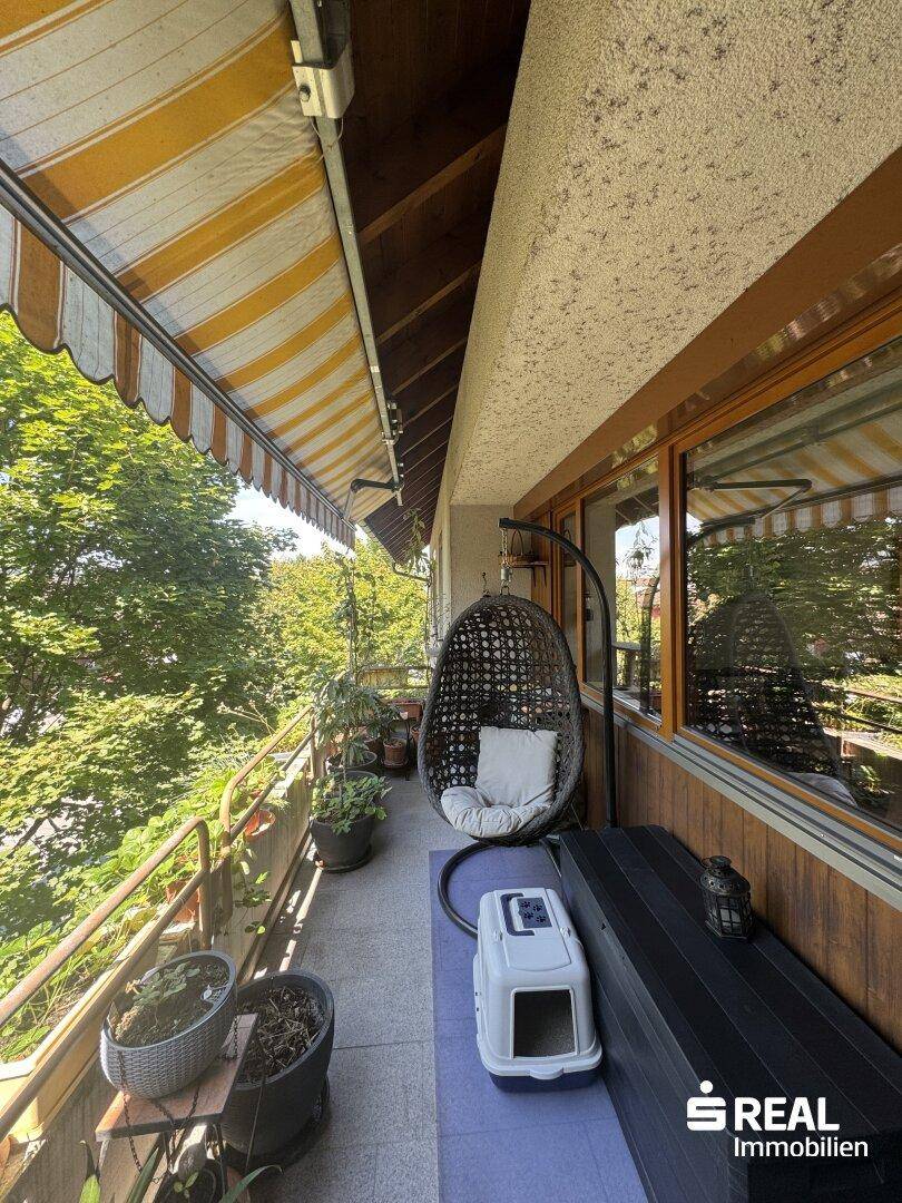 Heller Balkon mit gemütlichem Hängesessel und Sitzbank, umgeben von üppigem Grün.