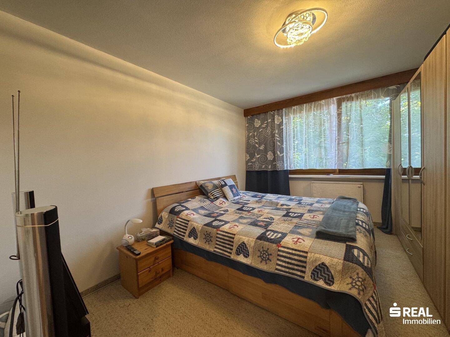Schlafzimmer mit Doppelbett, Holzmöbeln und einem Fenster mit Vorhängen.