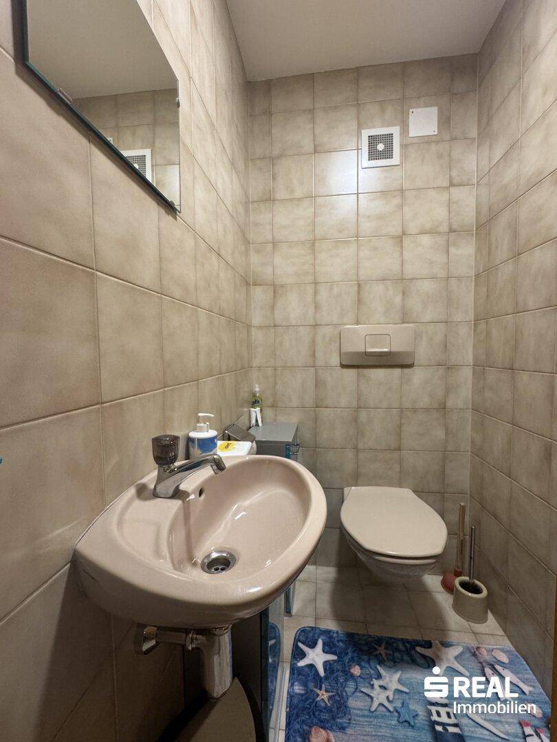 Kleines WC mit Toilette und Waschbecken, vollständig gefliest in hellen Farben.