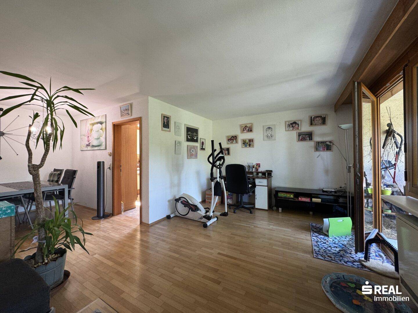 Heller Wohn-Essbereich mit Zugang zum Balkon, Fitnessgerät und einem Arbeitsbereich.