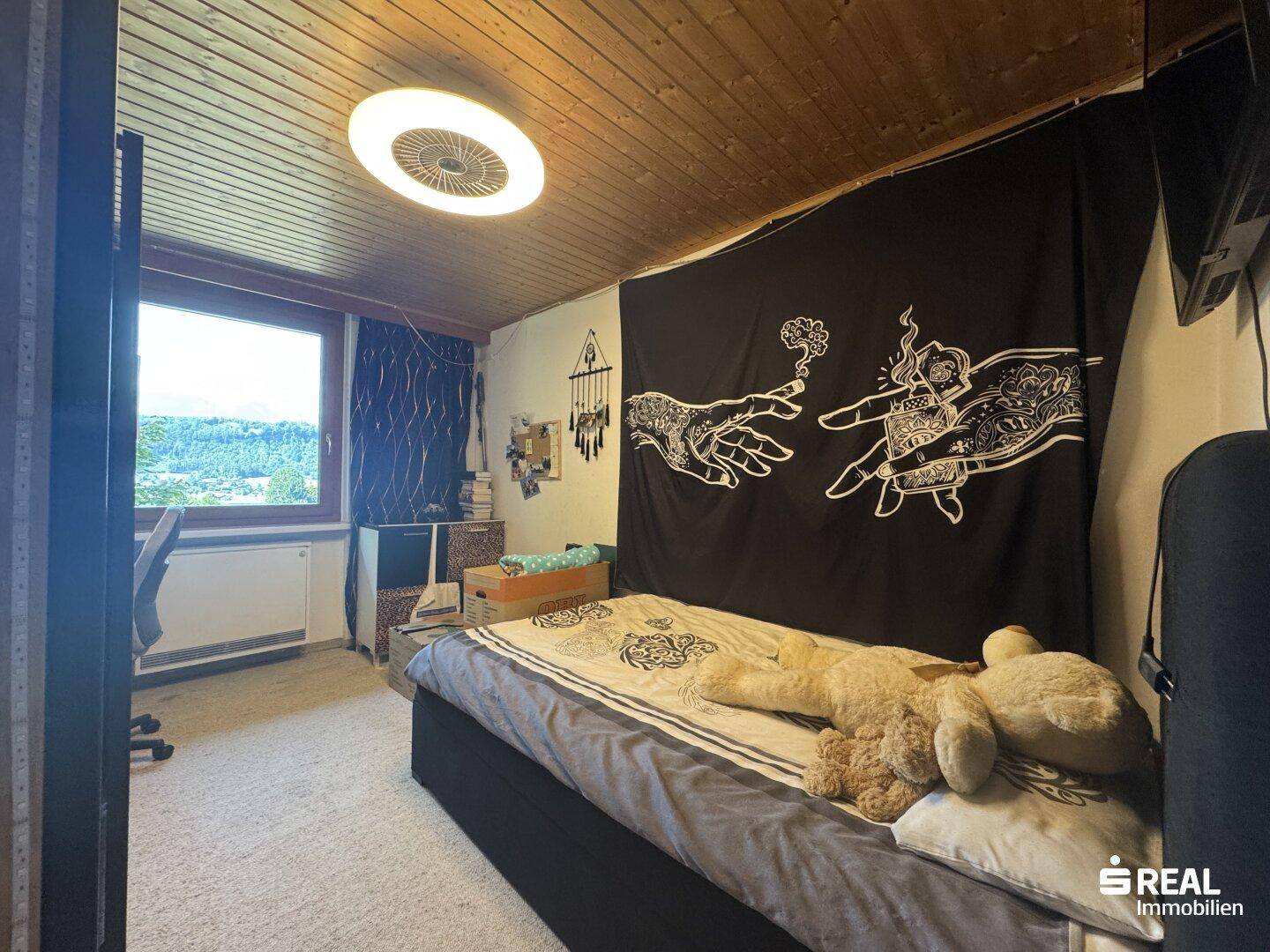 Schlafzimmer mit Einzelbett, Holzdecke und einem Fenster mit Blick ins Grüne.
