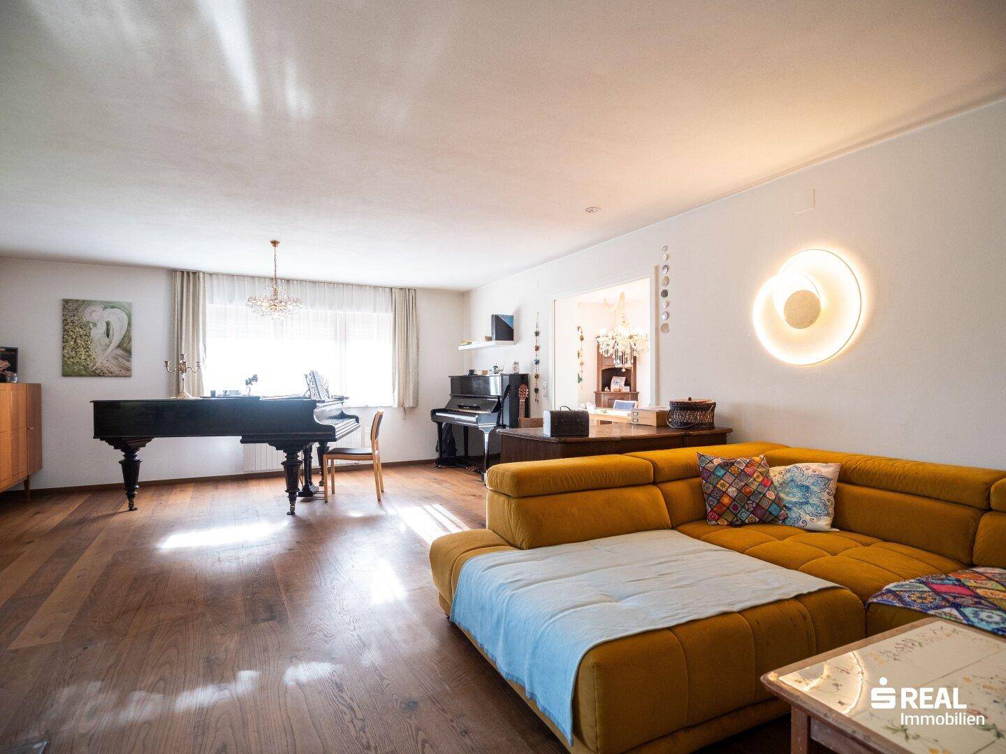 Großzügiges Wohnzimmer mit gelbem Sofa, Flügel und Holzboden, hell und einladend.