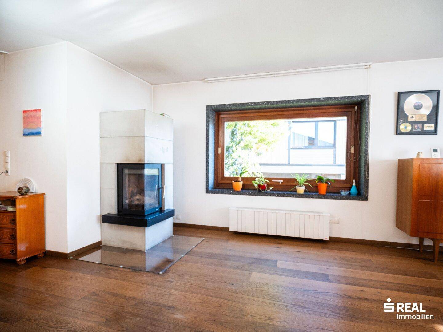 Wohnbereich mit modernem Kamin, großem Fenster und Blick ins Grüne.