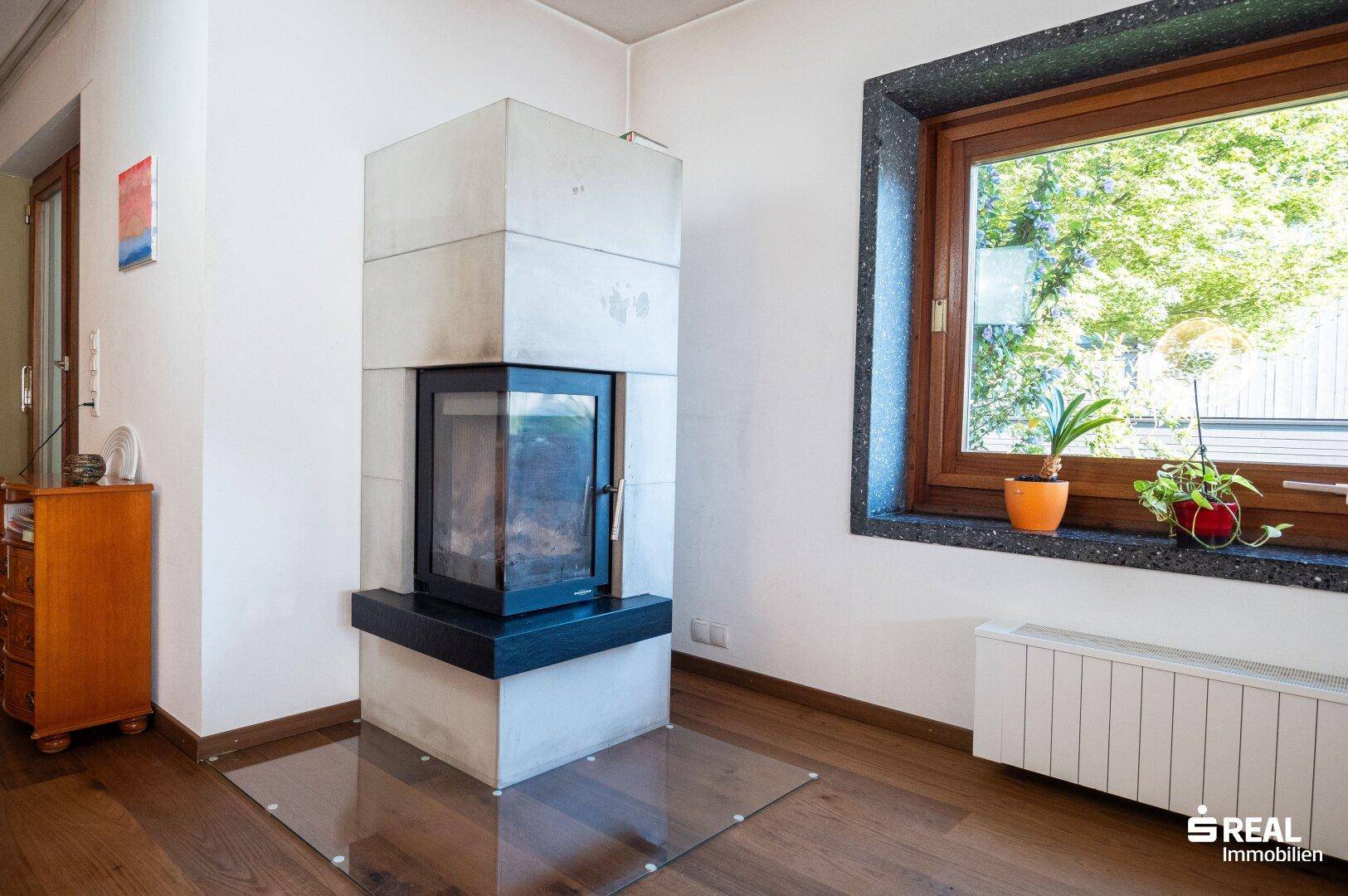 Detailansicht des modernen Kamins und des Fensters mit Pflanzen und Grünblick.