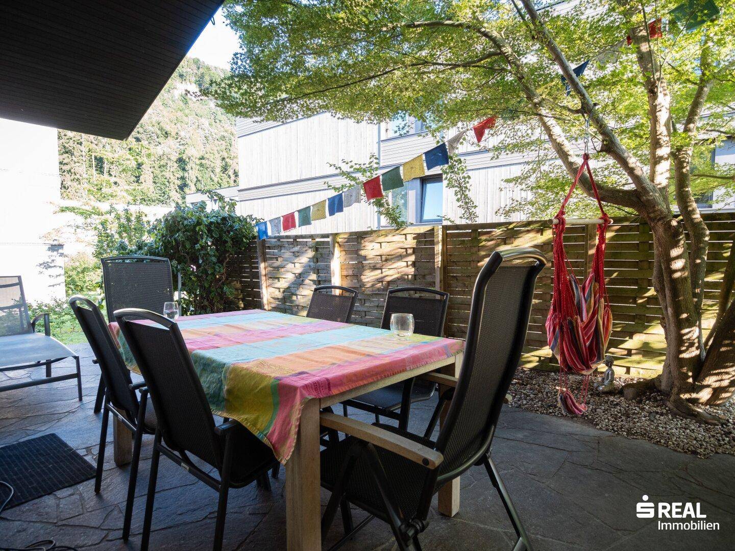 Gemütliche Terrasse mit Esstisch, Stühlen und Hängematte unter einem Baum.