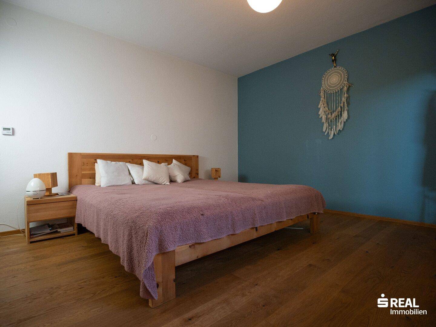 Schlafzimmer mit Holzbett, blauer Akzentwand und warmem Holzboden.