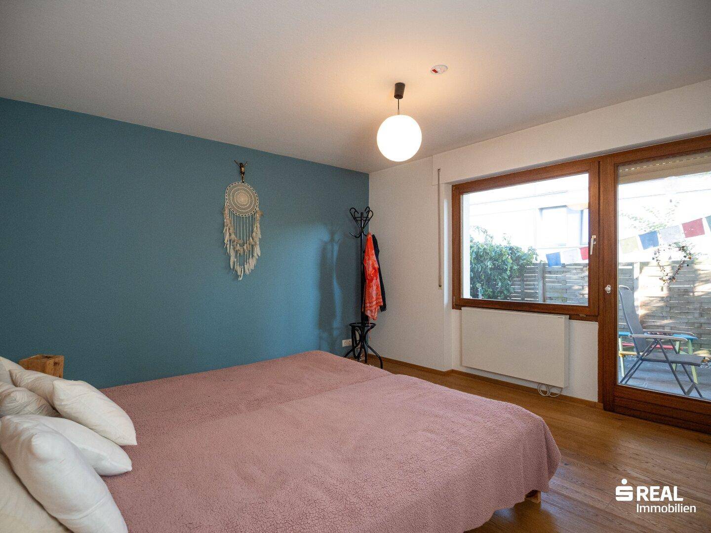 Helles Schlafzimmer mit Holzbett, blauer Wand und Zugang zum Außenbereich.