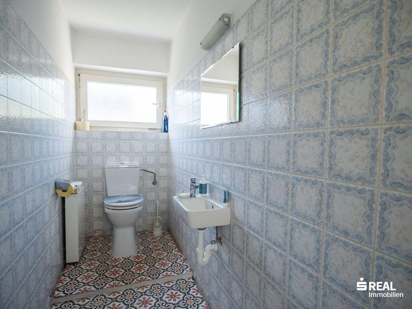 Kleines WC mit blau-weiß gemusterten Fliesen, Toilette und Waschbecken.