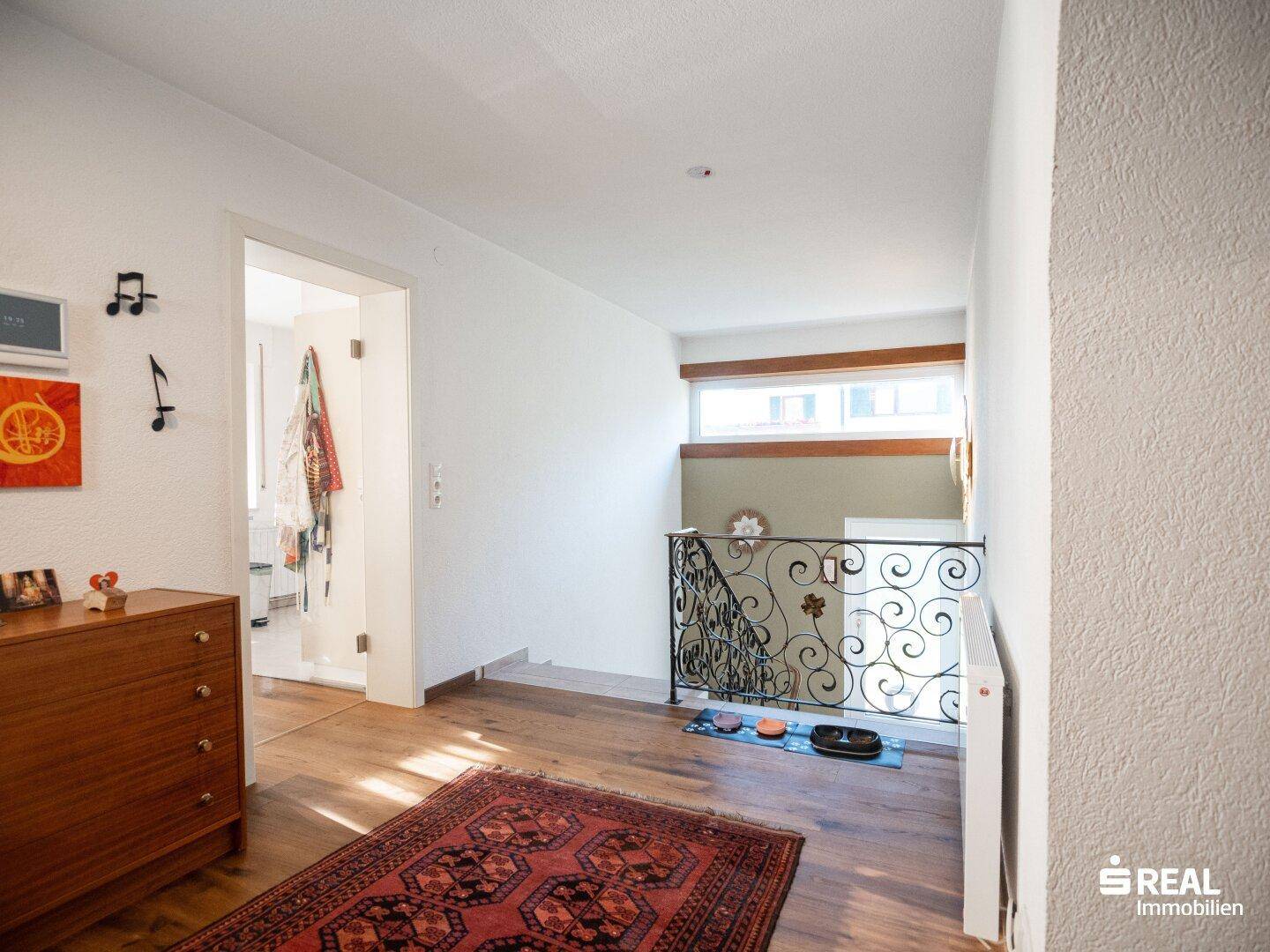 Geräumiger Flur mit Holzboden, Kommode und Zugang zu einem weiteren Zimmer.