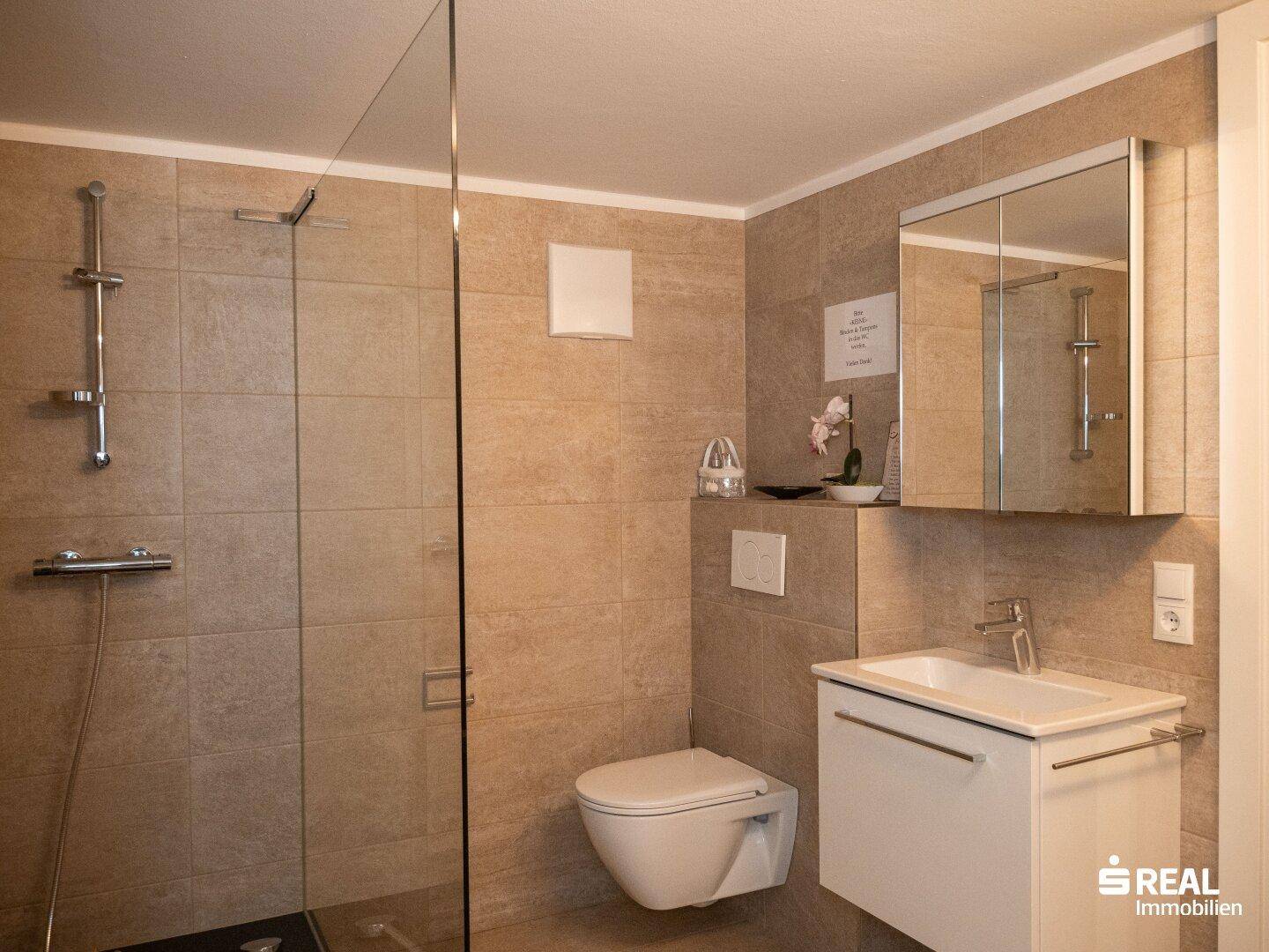 Modernes Badezimmer mit beigefarbenen Fliesen, ebenerdiger Dusche und wandhängendem WC.