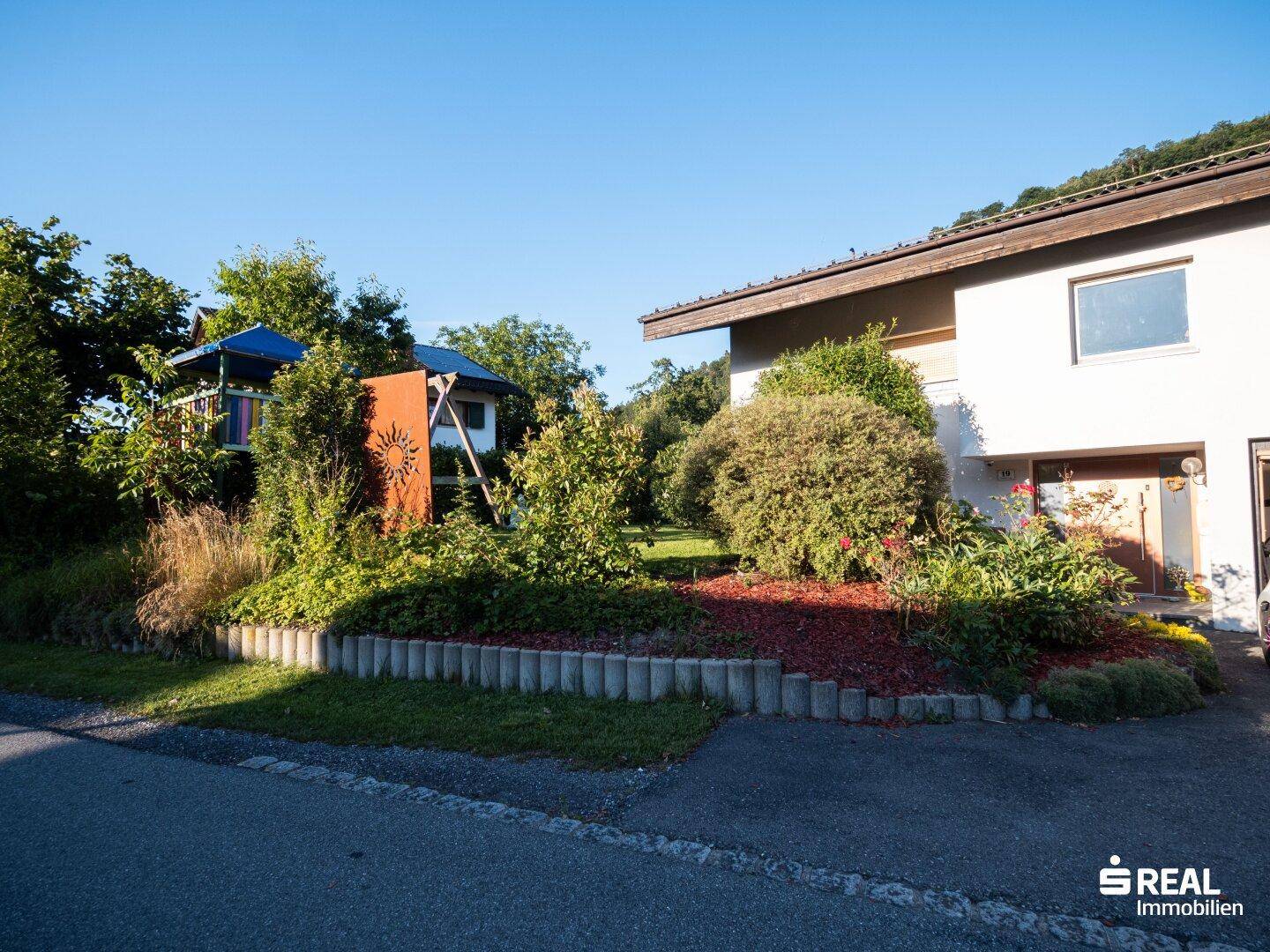 Vorderansicht des Hauses mit einem gepflegten Garten und einem kleinen Spielplatz für Kinder.