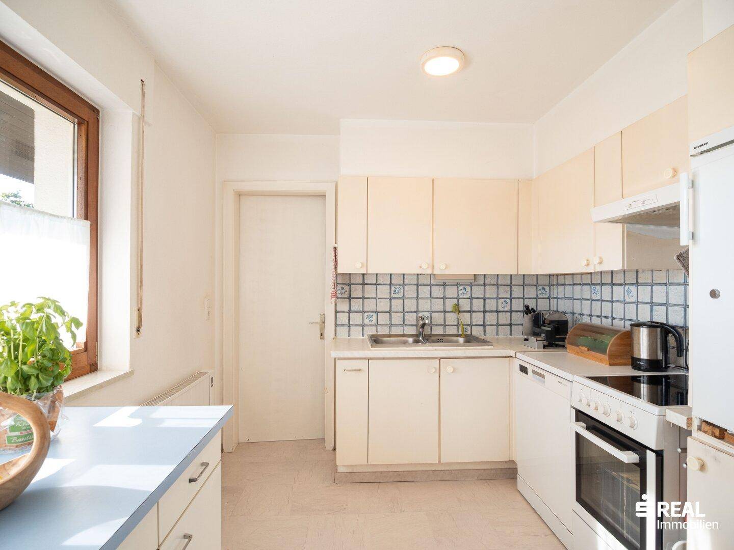Helle Küche mit beigen Schränken, Fliesenrückwand und einem Fenster für natürliches Licht.