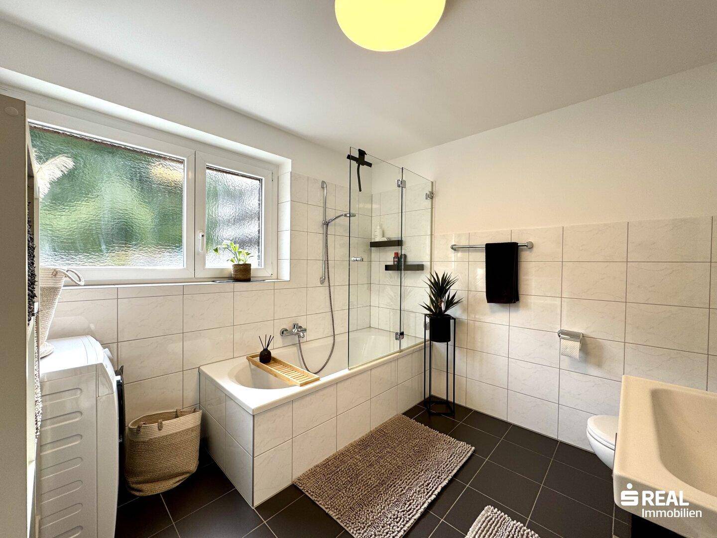Modernes Badezimmer mit Badewanne, Duschabtrennung und Fenster.
