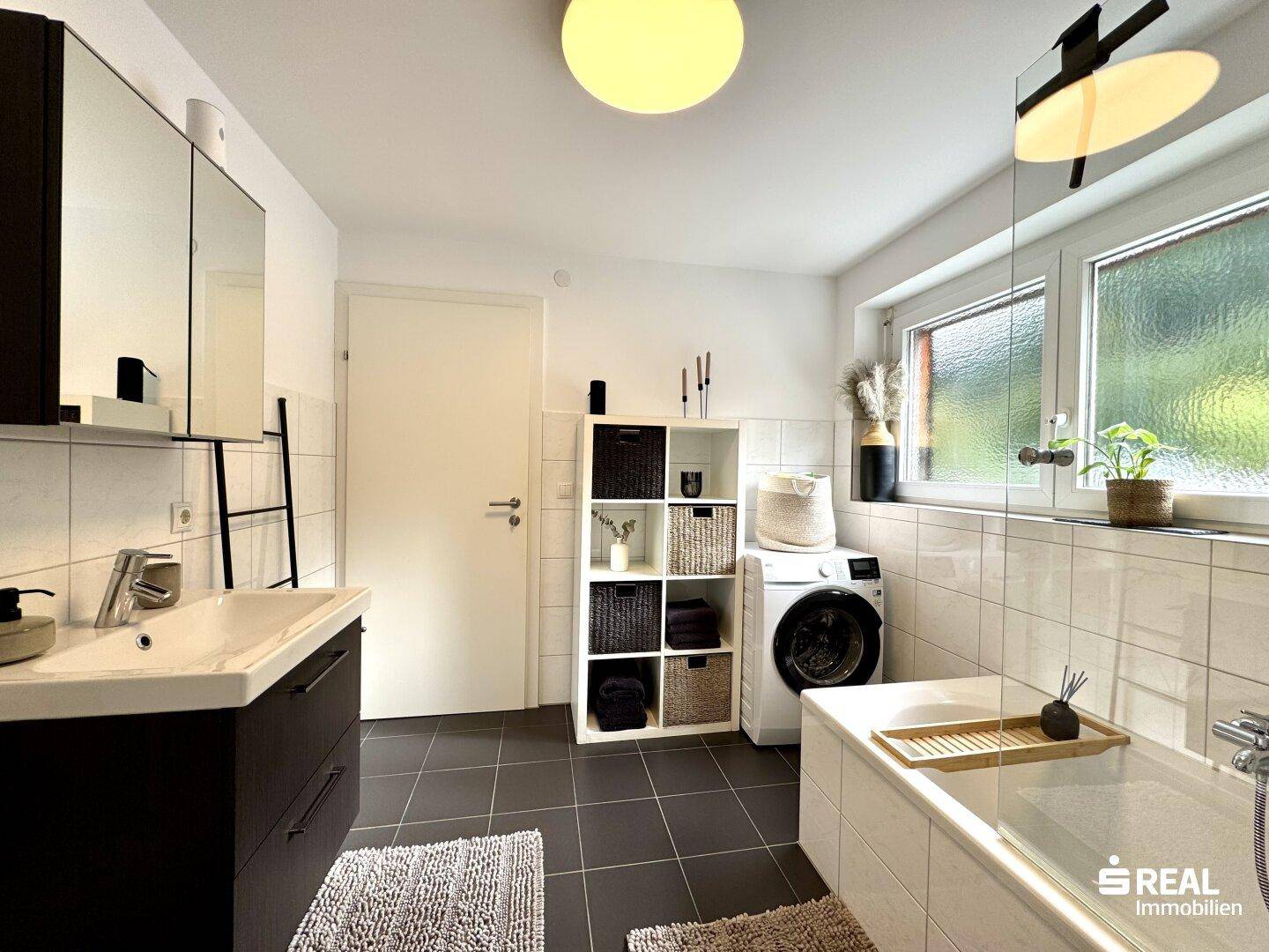 Modernes Badezimmer mit Badewanne, Waschmaschine und Fenster für Tageslicht.