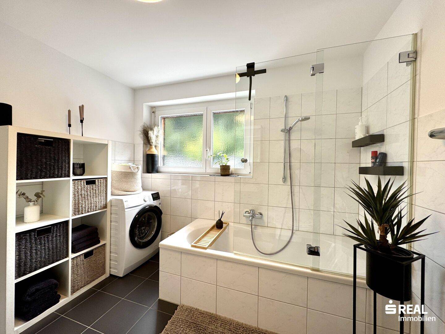 Badezimmer mit Badewanne, Duschabtrennung und Waschmaschine.
