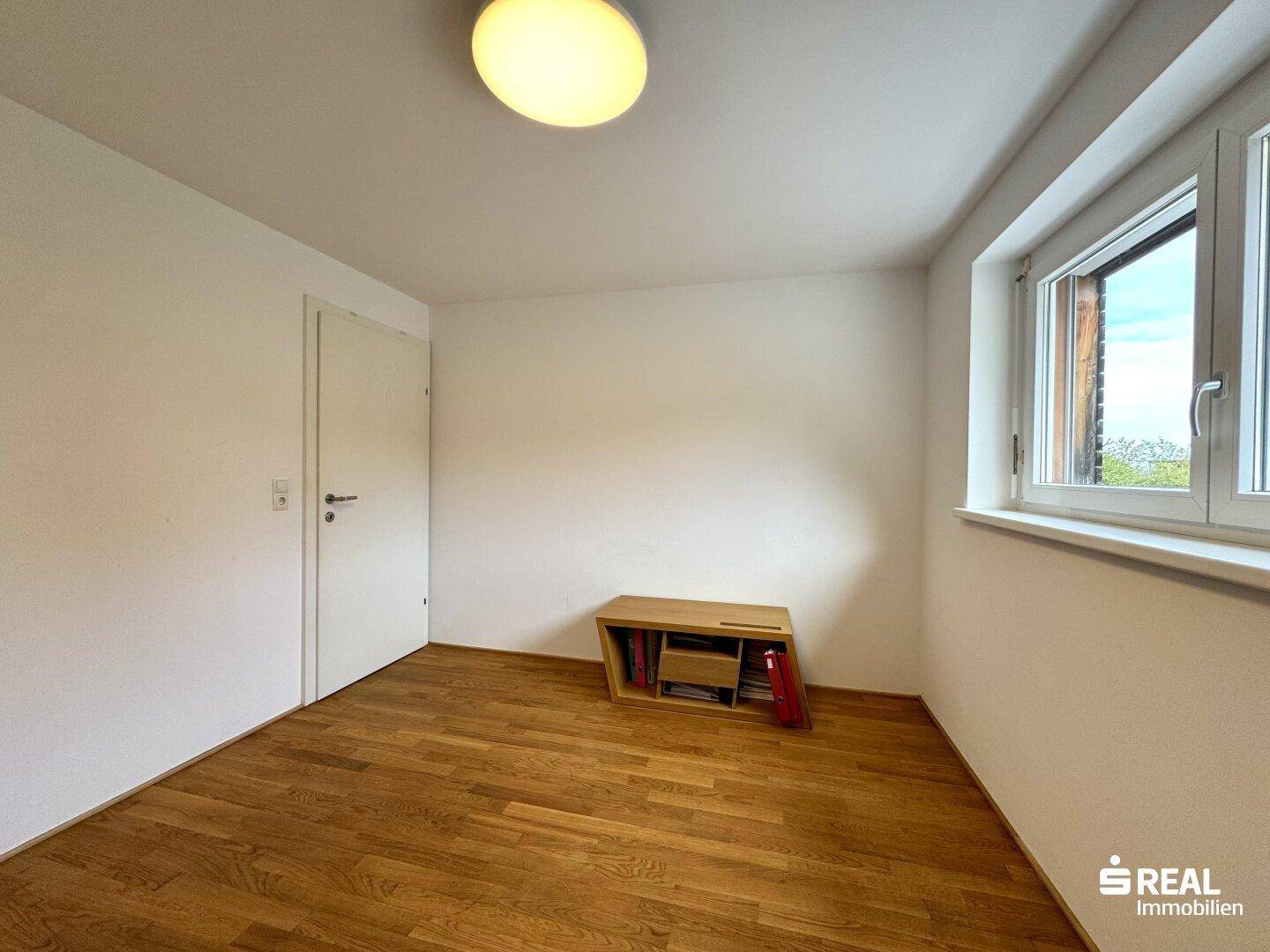 Leeres Zimmer mit Holzboden und Fenster, ideal als Kinder- oder Arbeitszimmer.