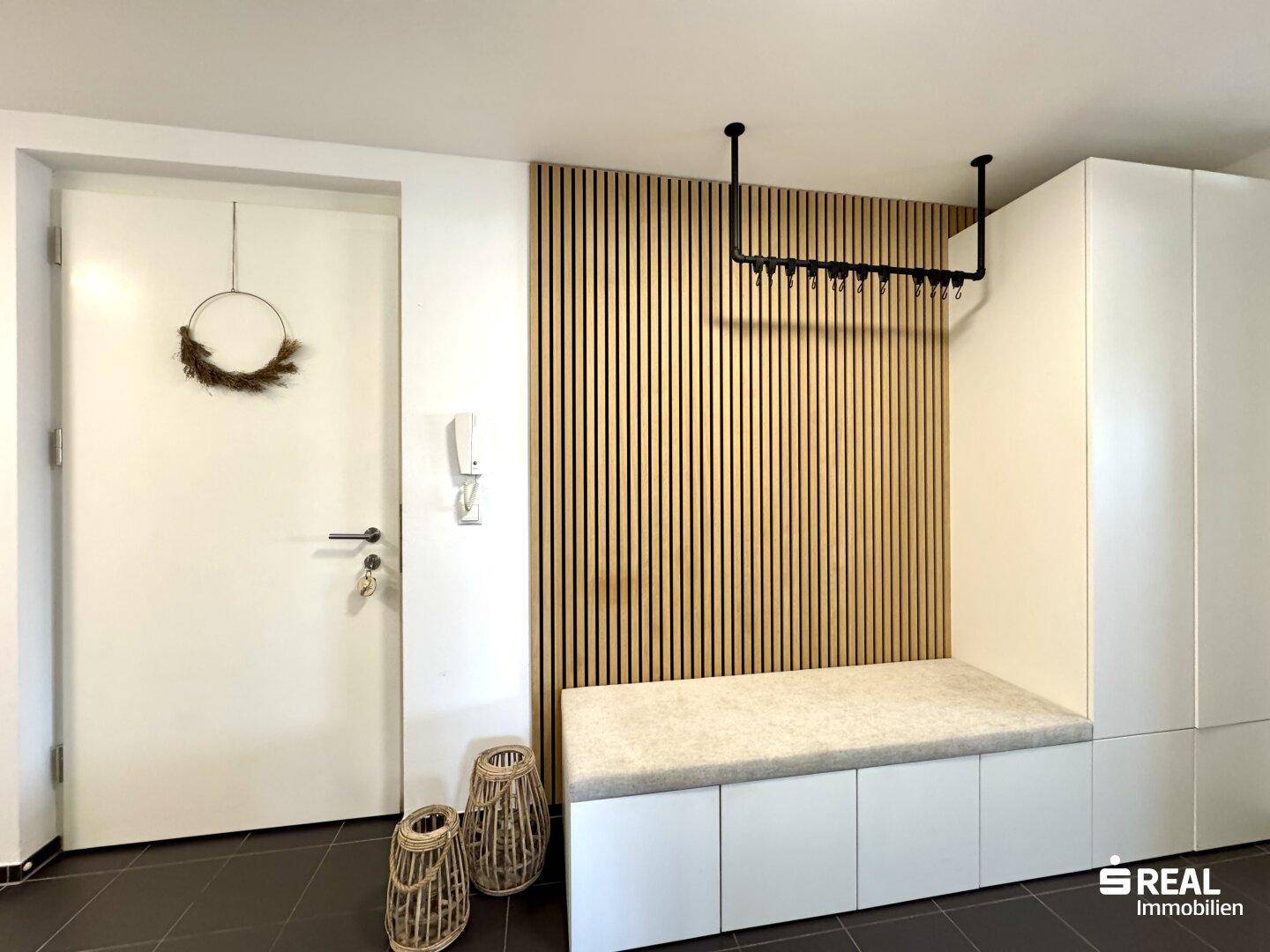Heller Eingangsbereich mit Holzlamellenwand, Sitzbank und Einbauschränken.