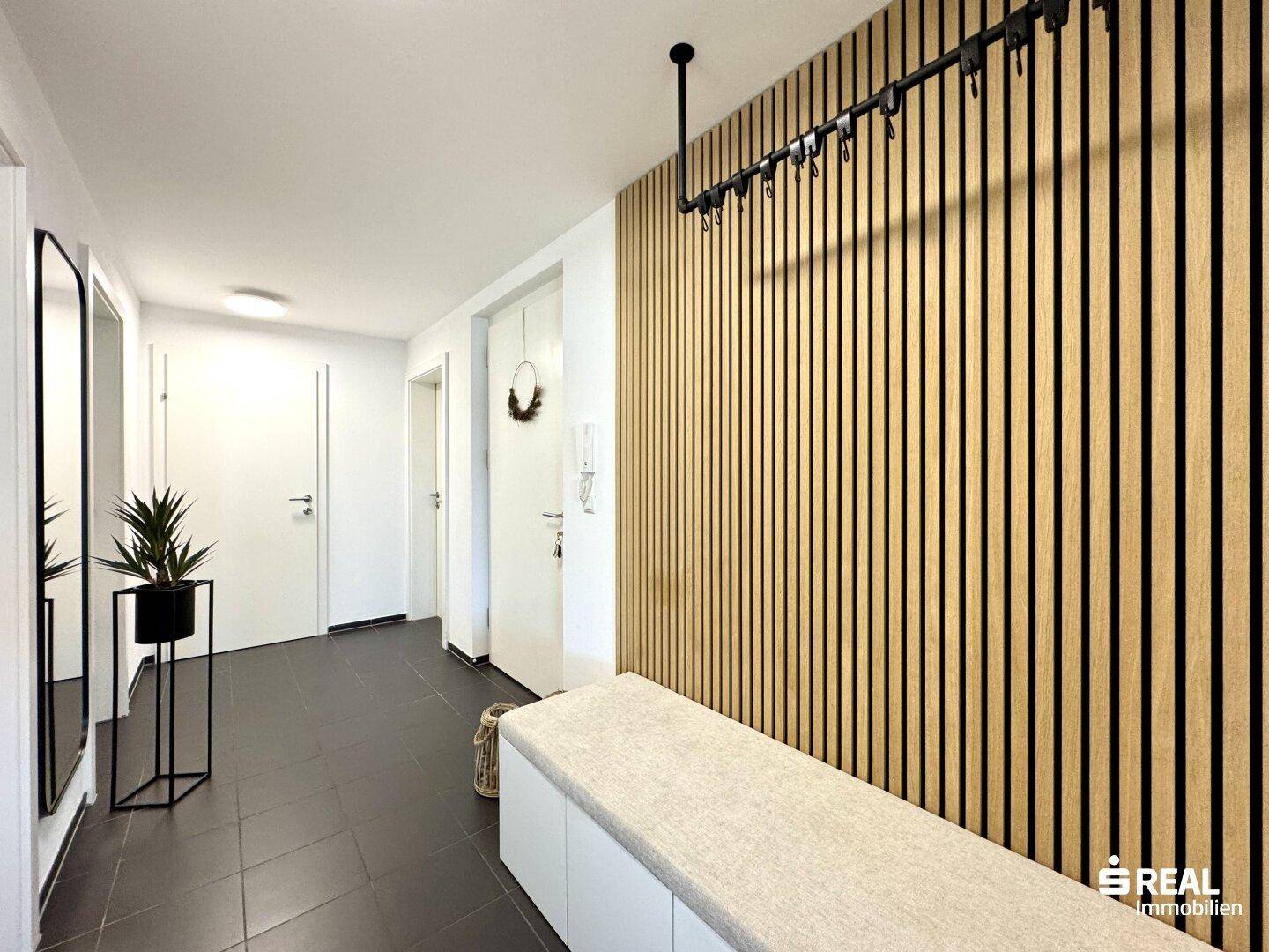 Moderner Eingangsbereich mit Holzlamellenwand, Sitzbank und integrierter Garderobe.