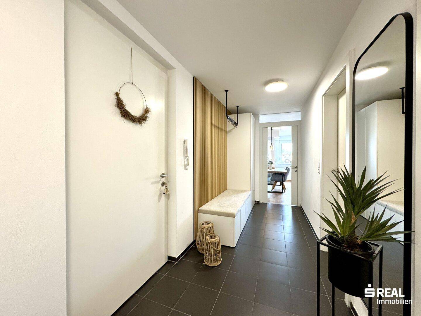 Heller Flur mit dunklen Fliesen, Garderobe und dekorativen Holzelementen.