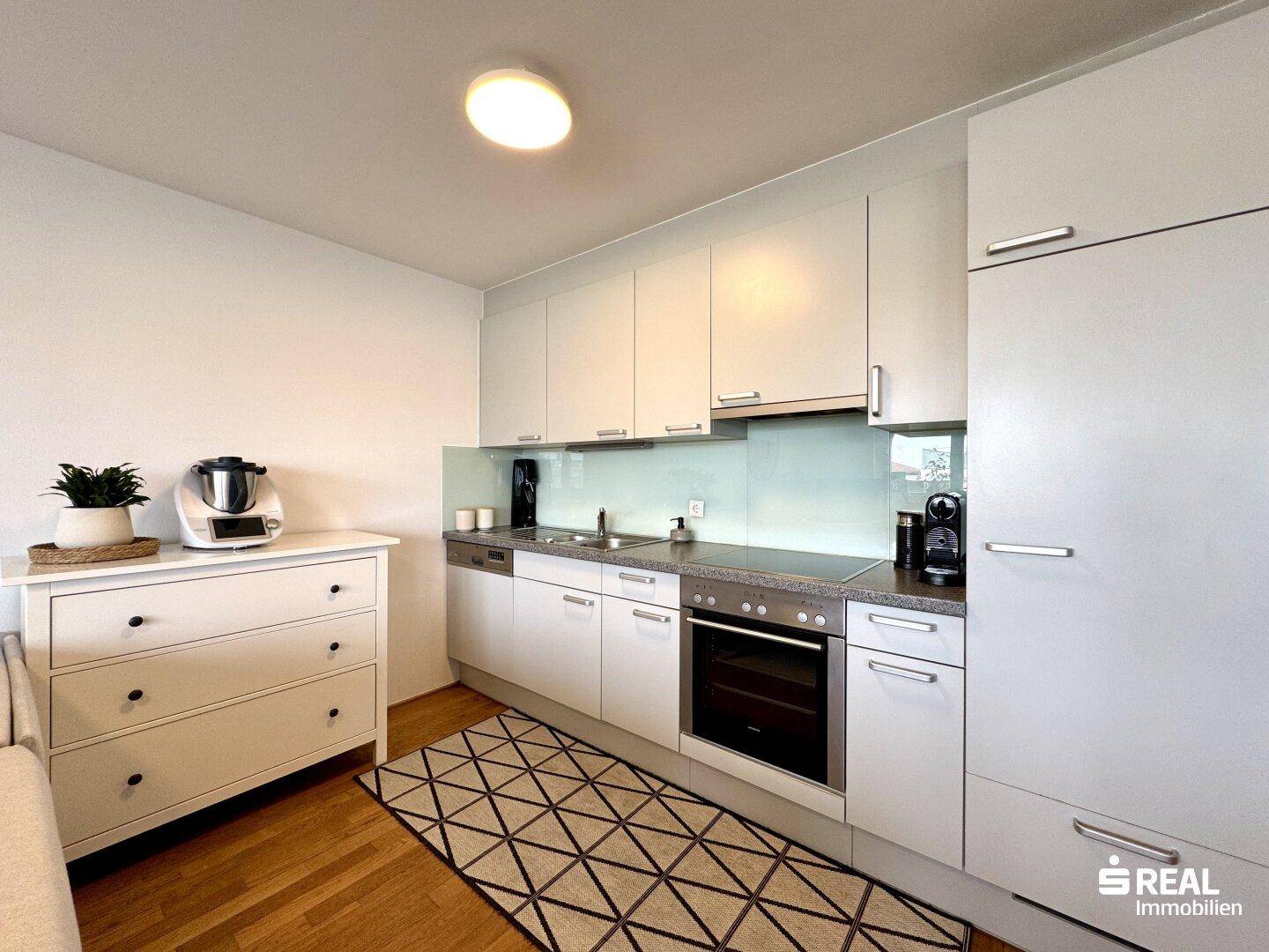 Moderne Einbauküche mit weißen Schränken, integrierten Geräten und Holzboden.