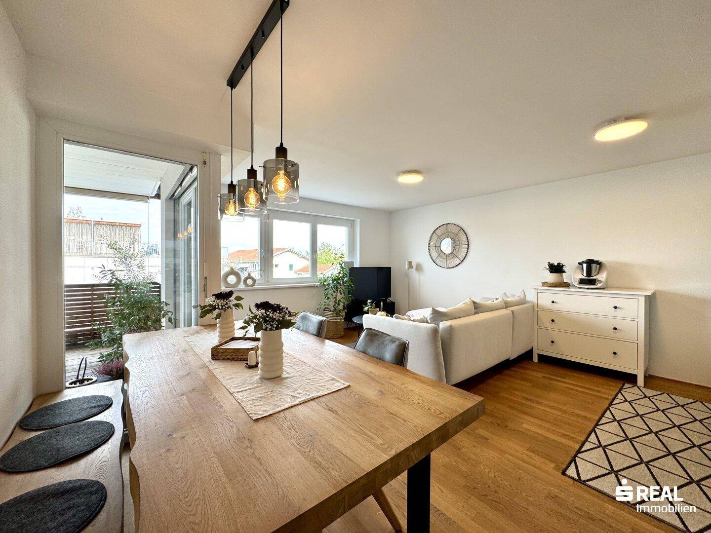 Heller Wohn- und Essbereich mit Holzboden, Sofa und Zugang zum Balkon.