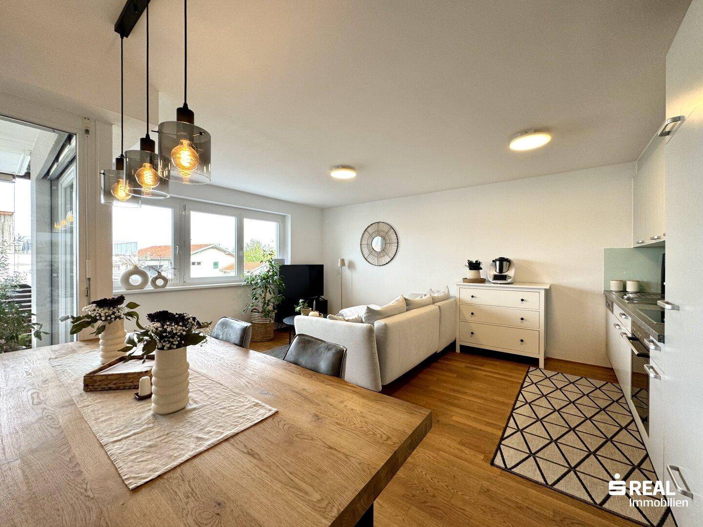 Offener Wohn- und Essbereich mit Holztisch, Sofa und moderner Küche.