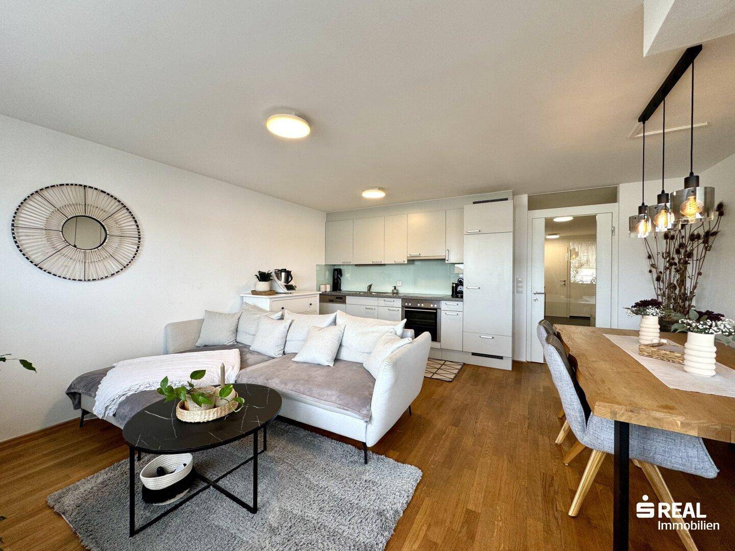 Offener Wohnbereich mit Sofa, Essbereich und integrierter moderner Küche.