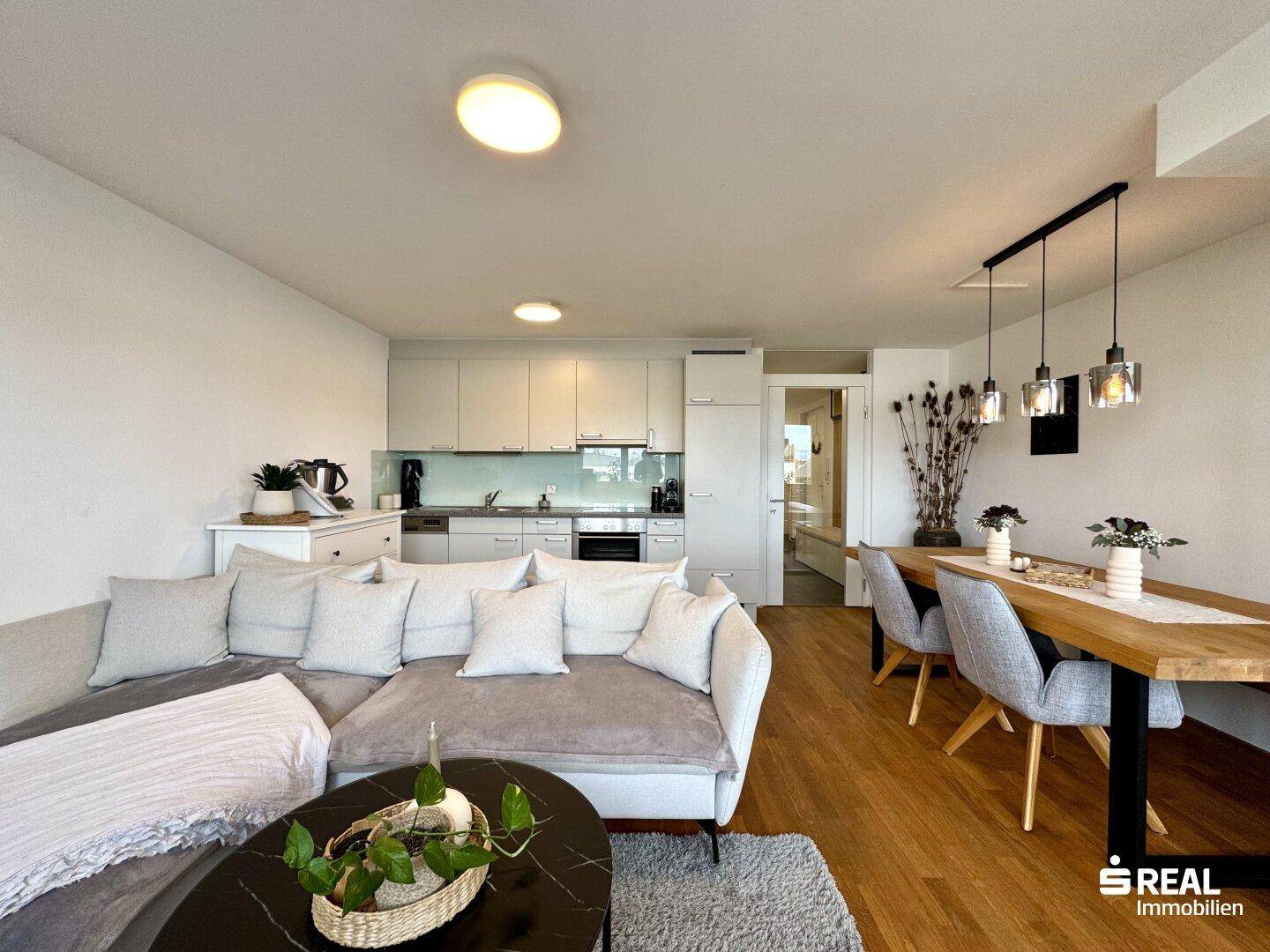Offener Wohnbereich mit Sofa, Essbereich und integrierter moderner Küche.