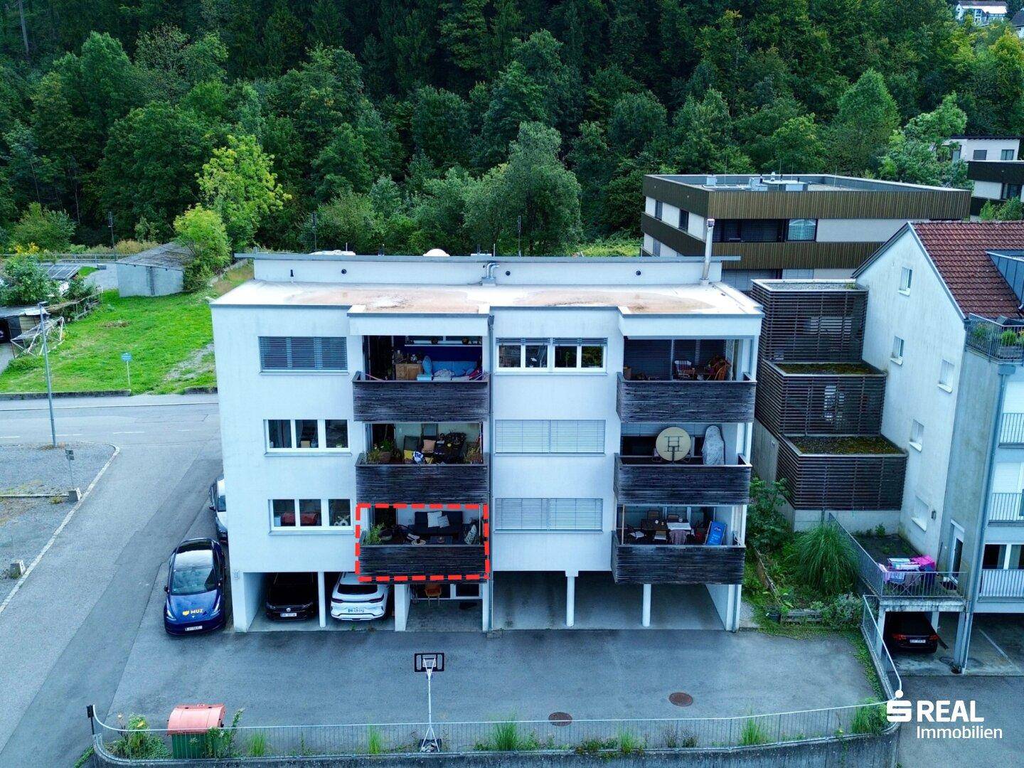 Mehrfamilienhaus mit Balkonen und umgebender Grünfläche.