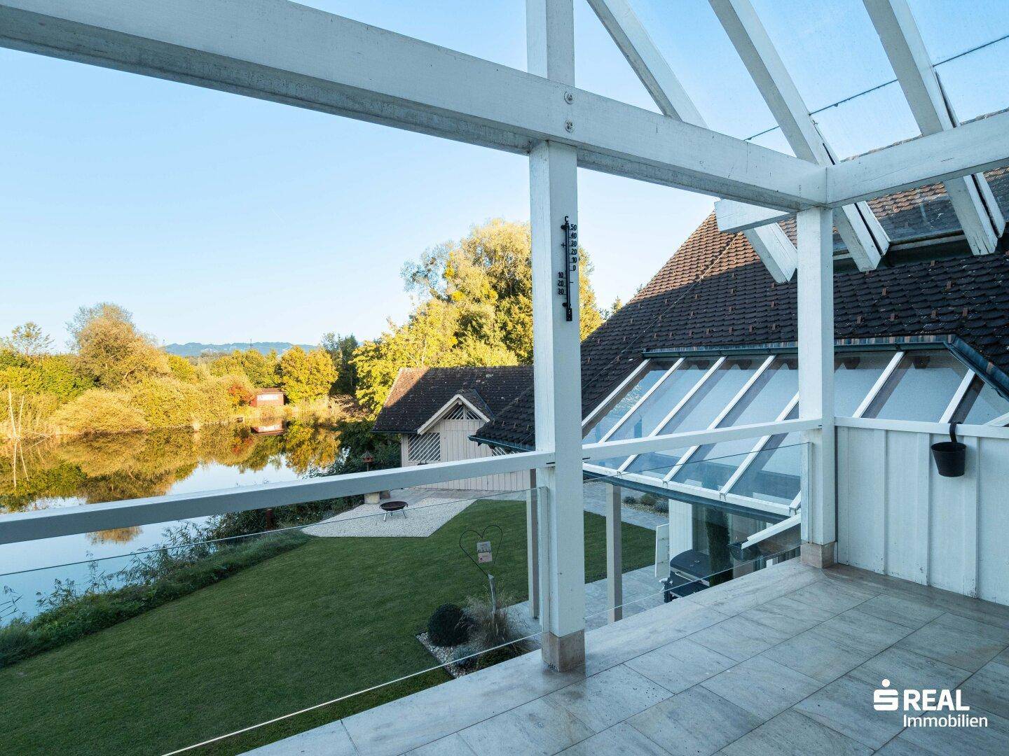 Überdachte Terrasse mit Fliesenboden und weitem Blick auf den See und die umliegende Natur.