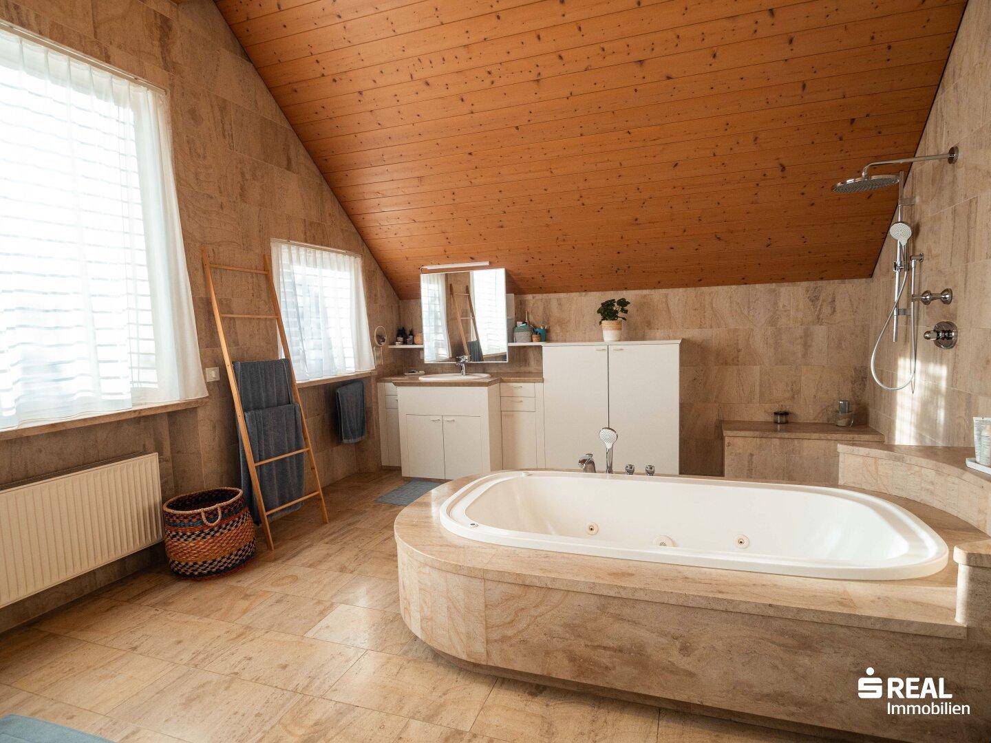 Geräumiges Badezimmer mit großer Badewanne, Dusche und holzverkleideter Dachschräge.