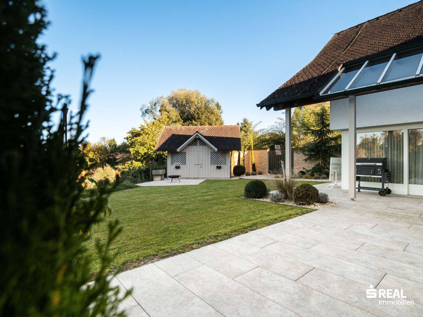 Gepflegter Garten mit Rasenfläche, Terrasse und einem charmanten Gartenschuppen.