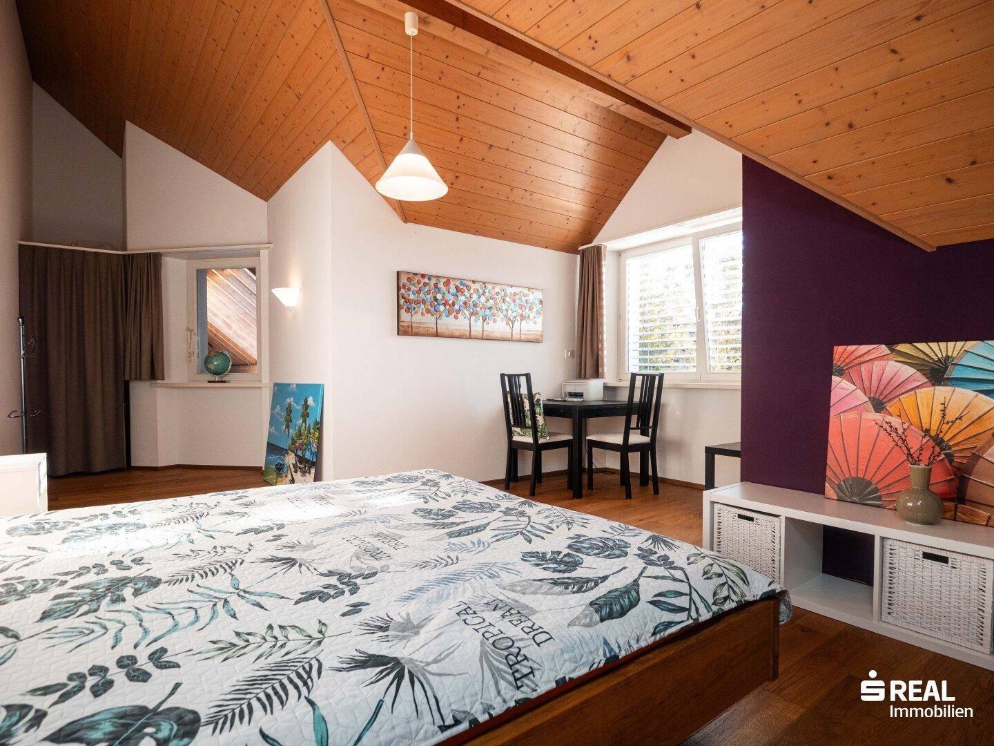 Helles Schlafzimmer mit Holzboden, Dachschräge und einem kleinen Arbeitsbereich.