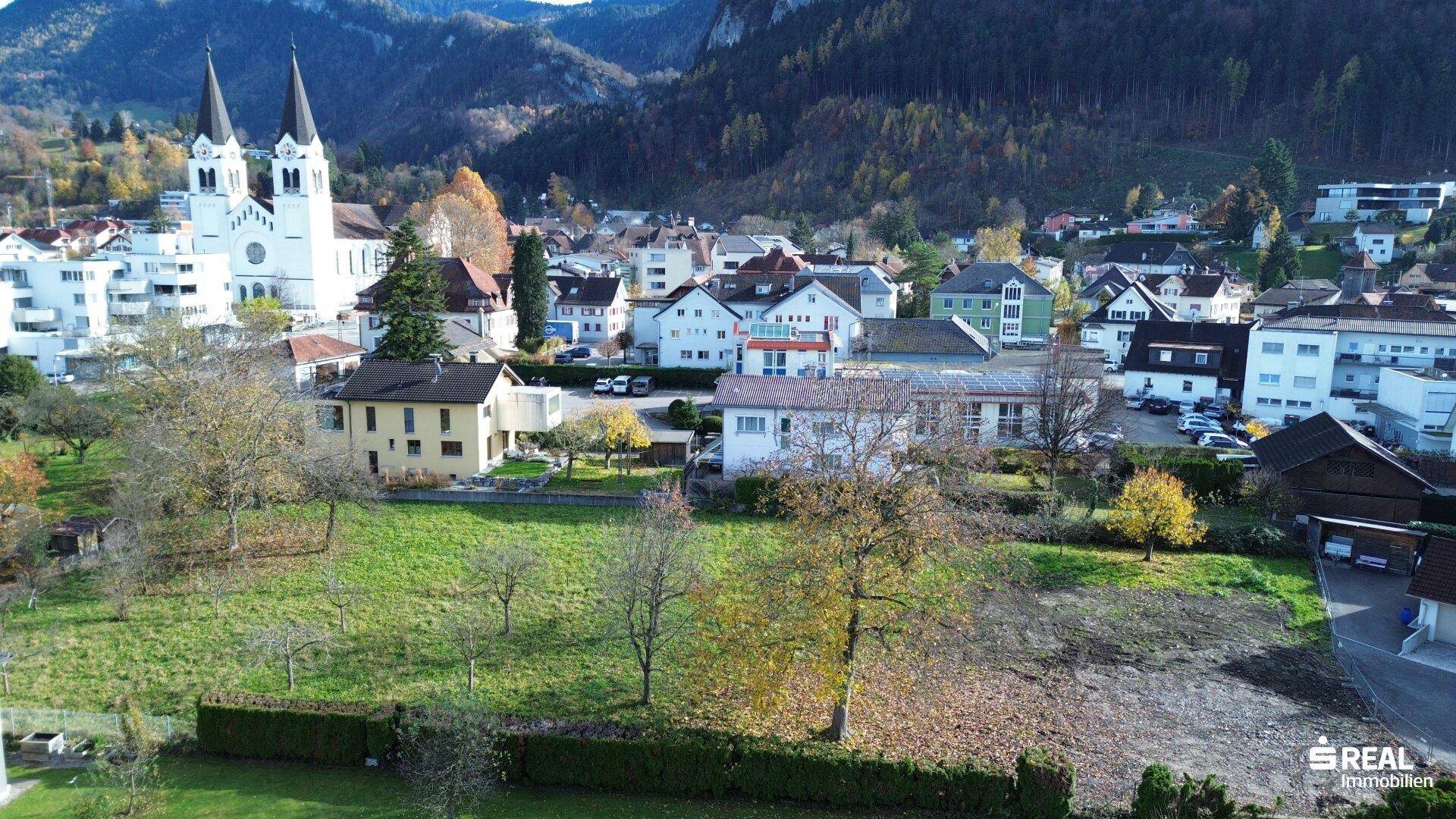 Luftaufnahme einer Wohngegend mit viel Grün, einer Kirche und Häusern mit Solaranlagen auf den Dächern.