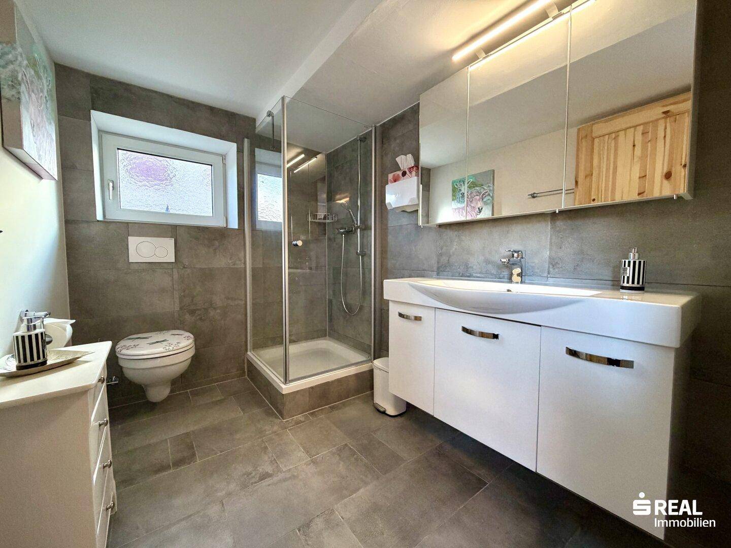 Modernes Badezimmer mit Dusche, Waschtisch und Spiegelschrank, ausgestattet mit grauen Fliesen.