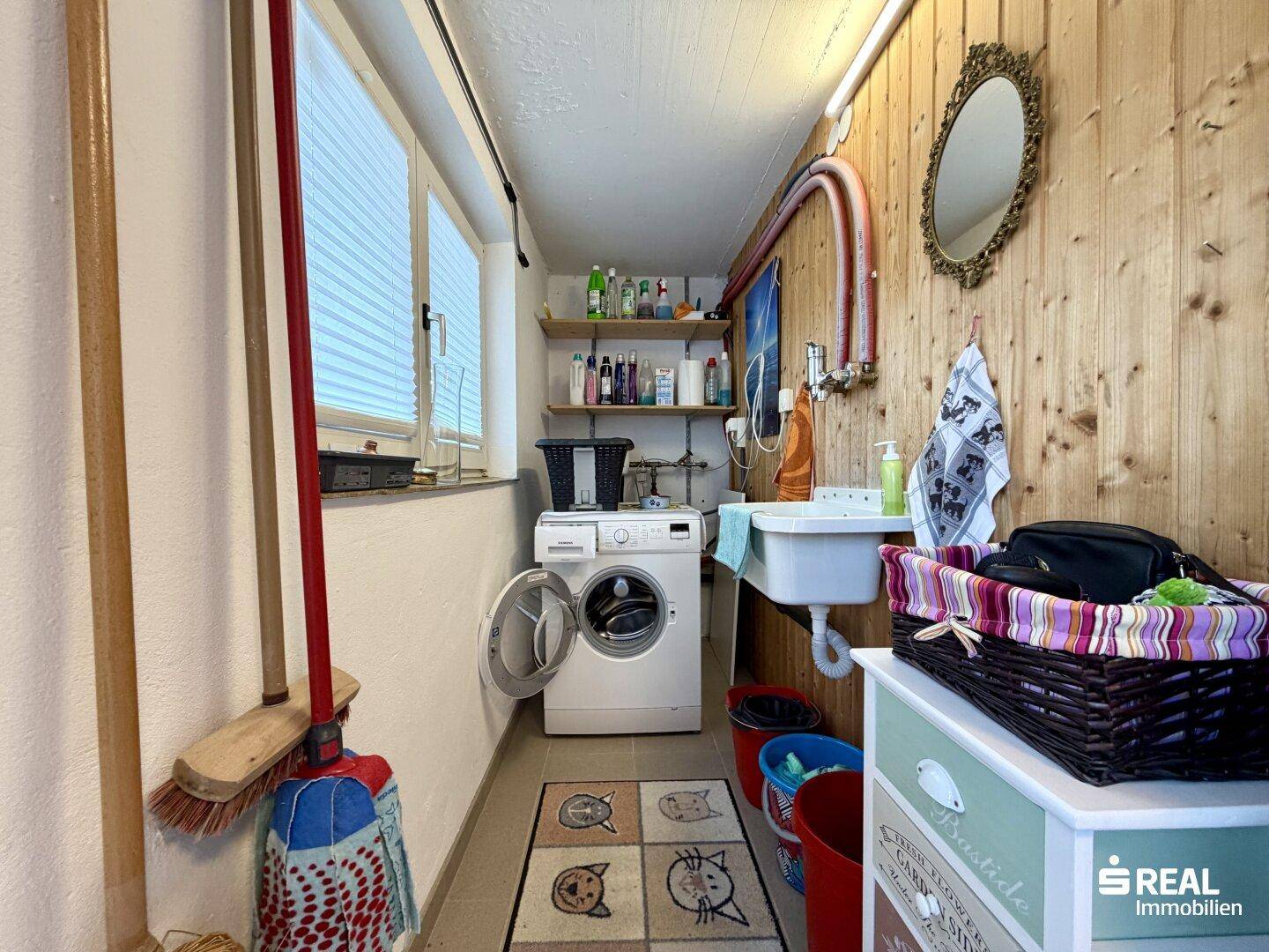 Praktischer Hauswirtschaftsraum mit Waschmaschine, Spülbecken und Holzverkleidung an den Wänden.