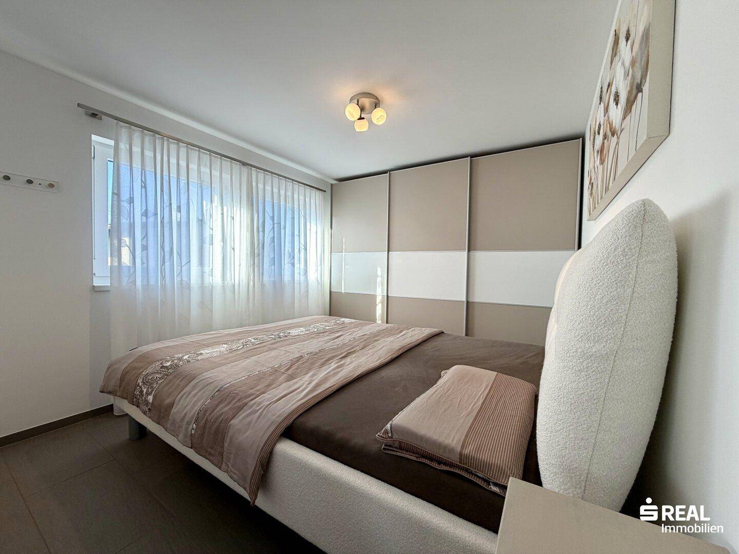 Schlafzimmer mit großem Bett, Einbauschränken und Fenster mit Vorhängen für Privatsphäre.