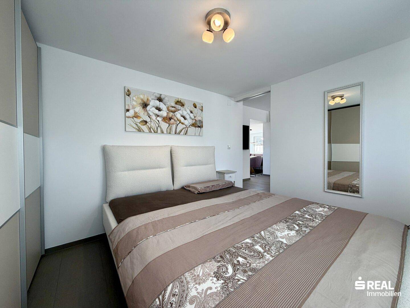 Helles Schlafzimmer mit Doppelbett, moderner Kunst an der Wand und Spiegel.