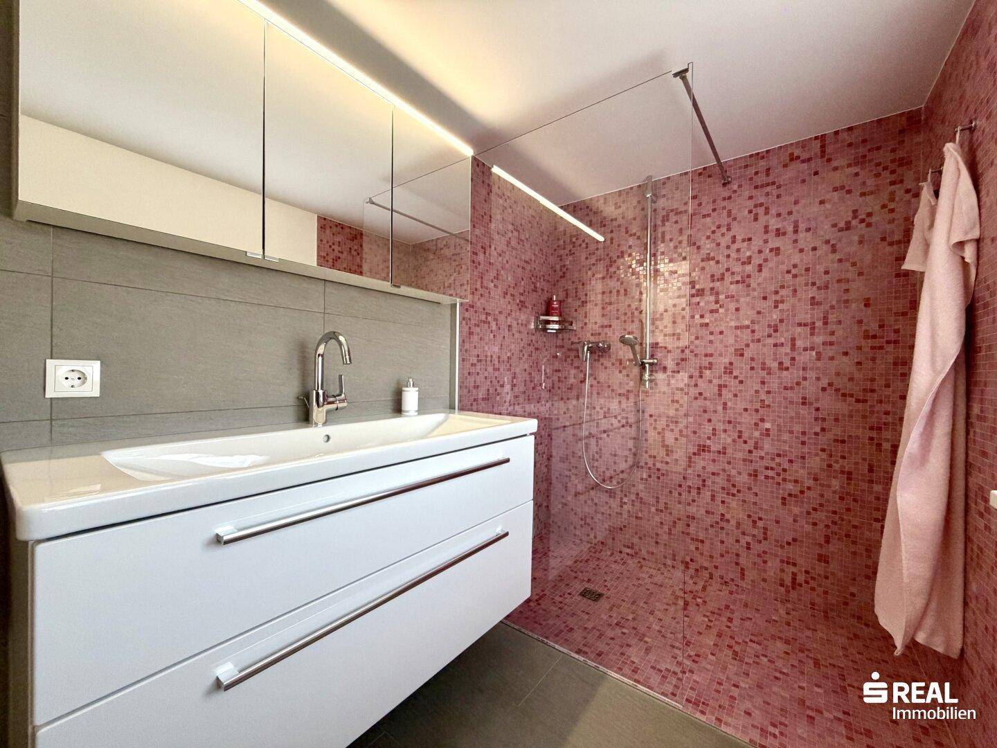 Modernes Badezimmer mit Waschtisch, Spiegelschrank und großer begehbarer Dusche mit Mosaikfliesen.
