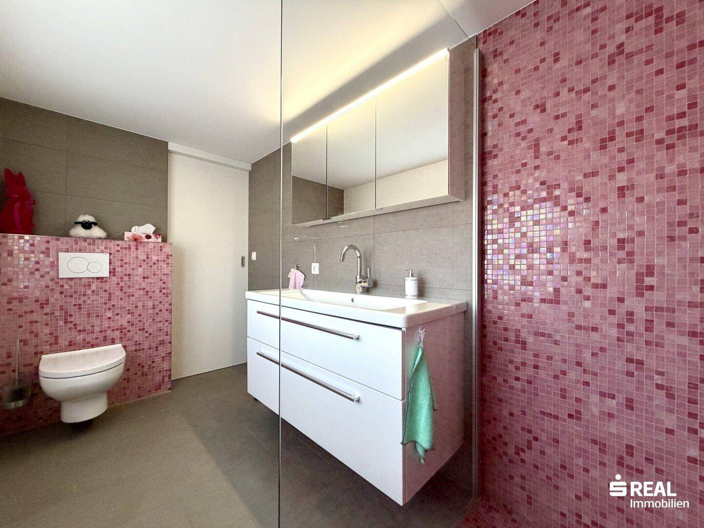 Stilvolles Badezimmer mit modernen Armaturen, Hänge-WC und farbigen Mosaikfliesen in der Dusche.
