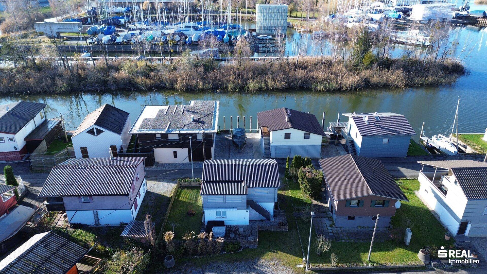 Luftaufnahme der Häuser am Wasser mit Bootsanlegern und umliegender Natur.