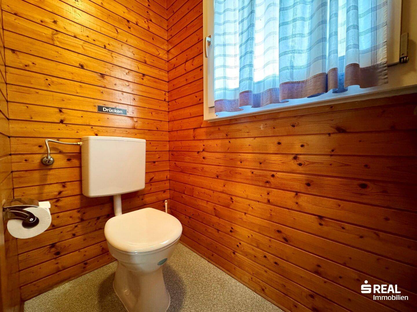 Kleines WC mit Holzvertäfelung, Fenster und einfacher Toilette.