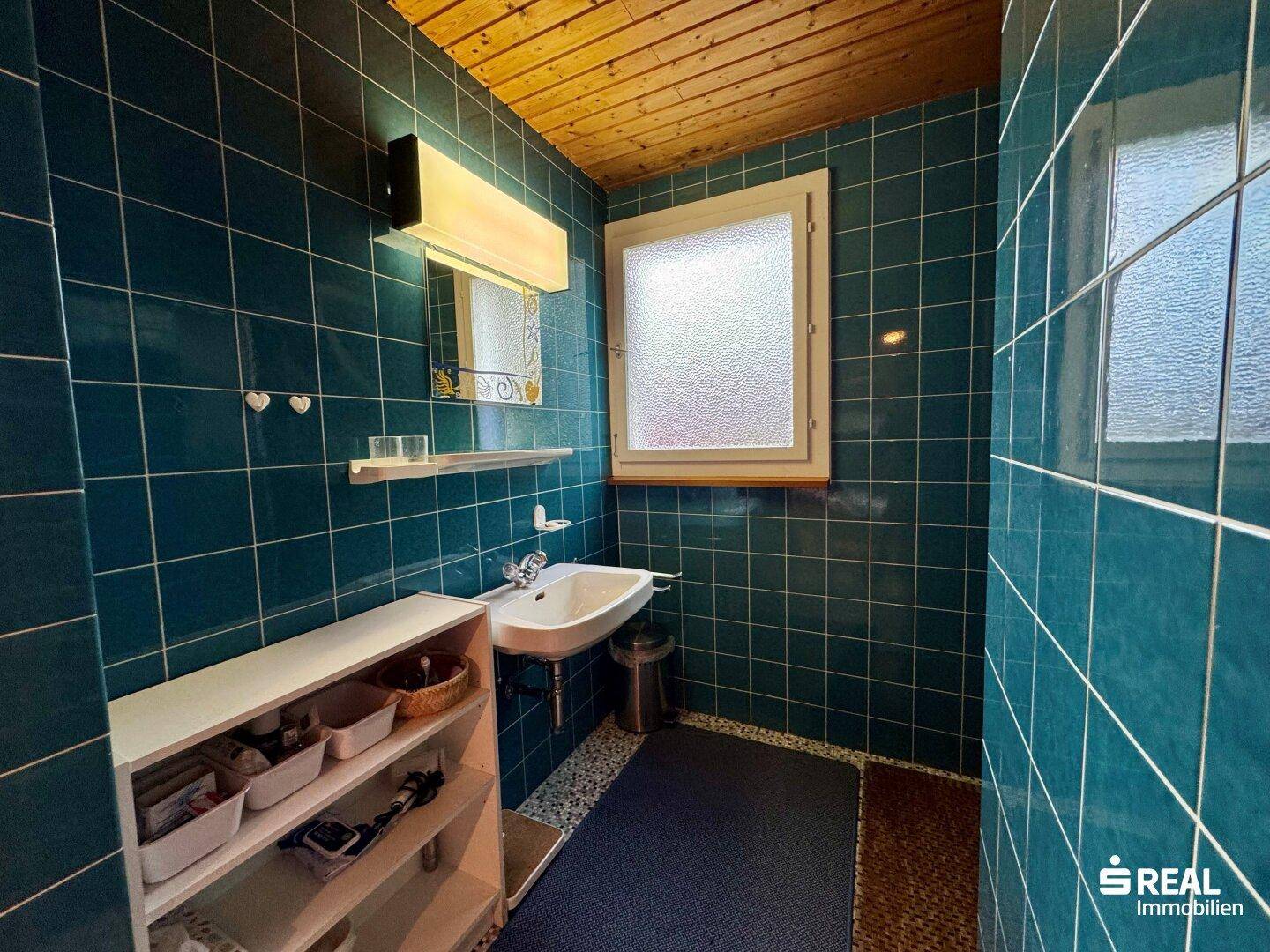 Badezimmer mit blauen Fliesen, Waschbecken und Fenster.