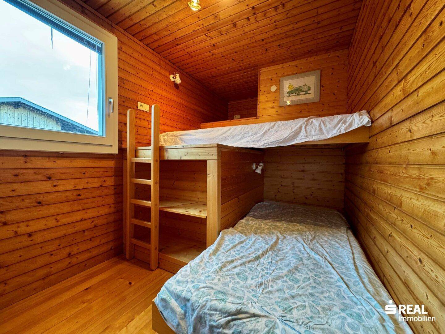Gemütliches Schlafzimmer mit Holzvertäfelung, Etagenbett und Einzelbett.